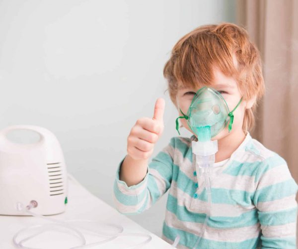 Little boy making inhalation with nebulizer at home.